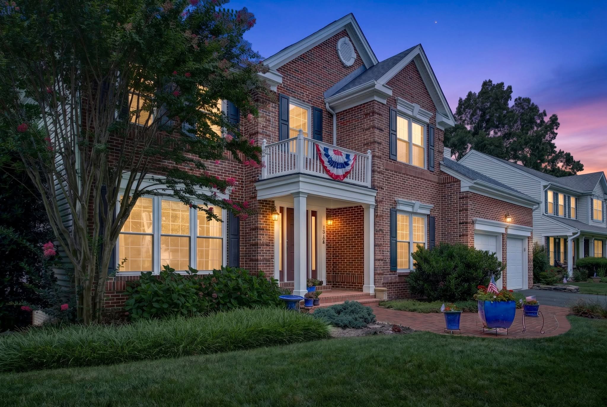 Brick colonial home with a second-story balcony photographed at twilight