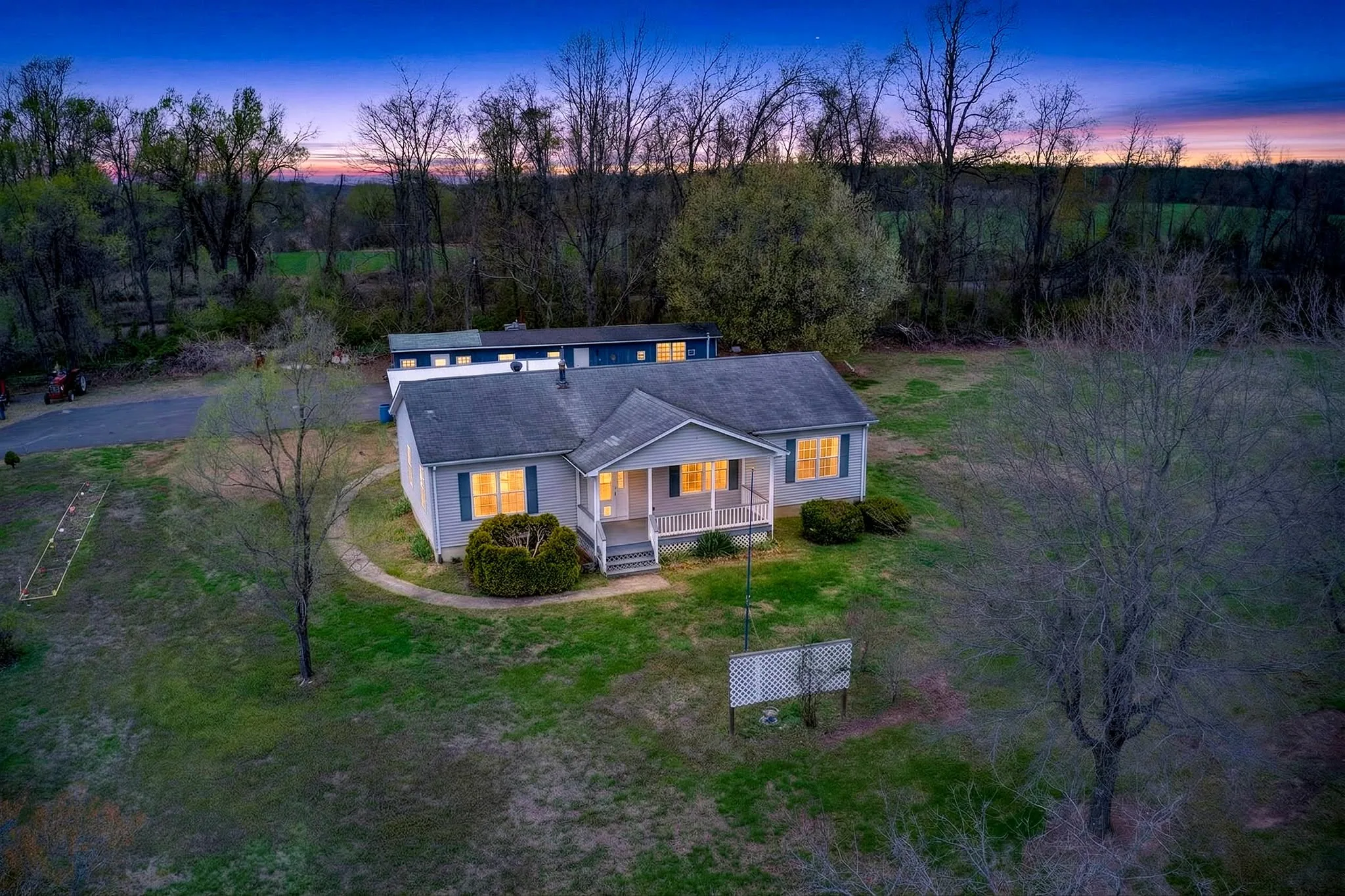 Virtual Twilight image of a single-story ranch home with lit windows across an open lawn under a deep dusk sky