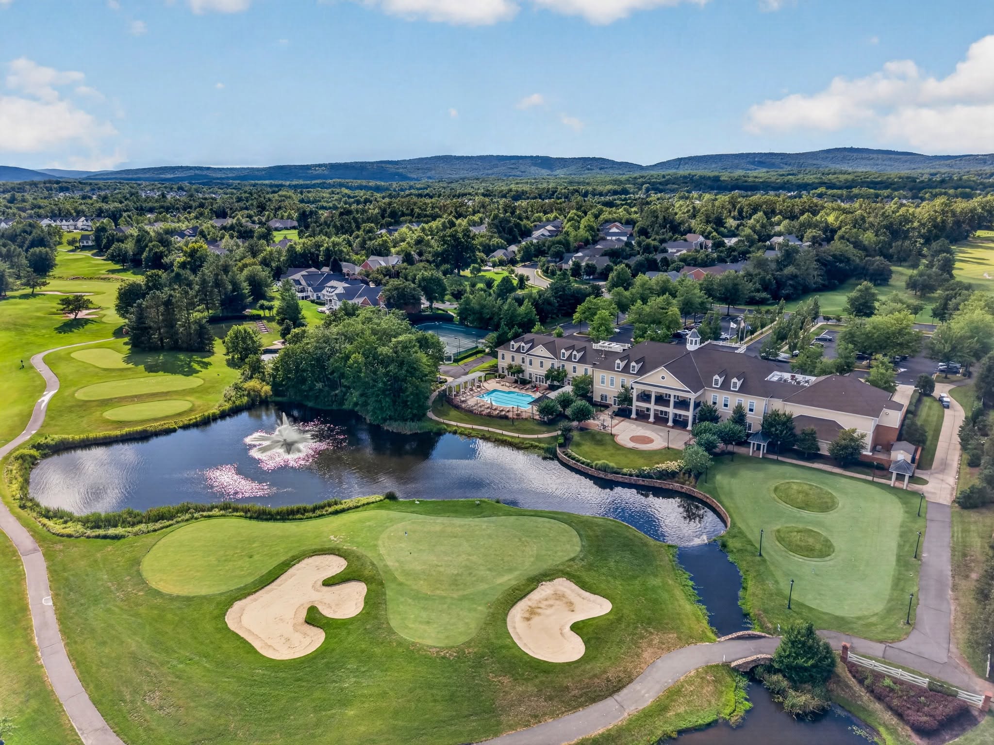 Aerial view of a golf clubhouse beside a pond with a fountain and distant mountains