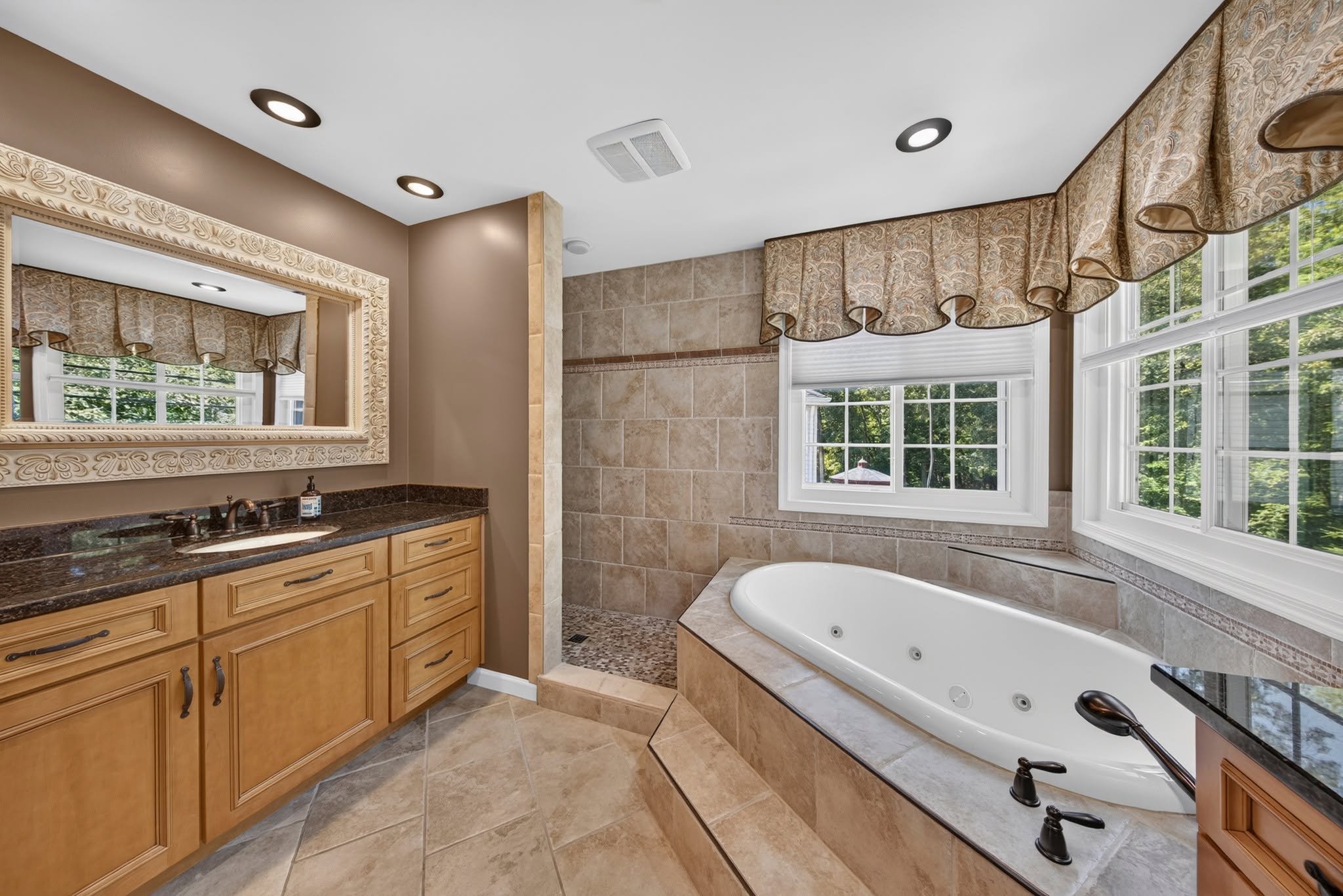 Primary bathroom with a corner jetted tub, tan tile surround and a glass shower