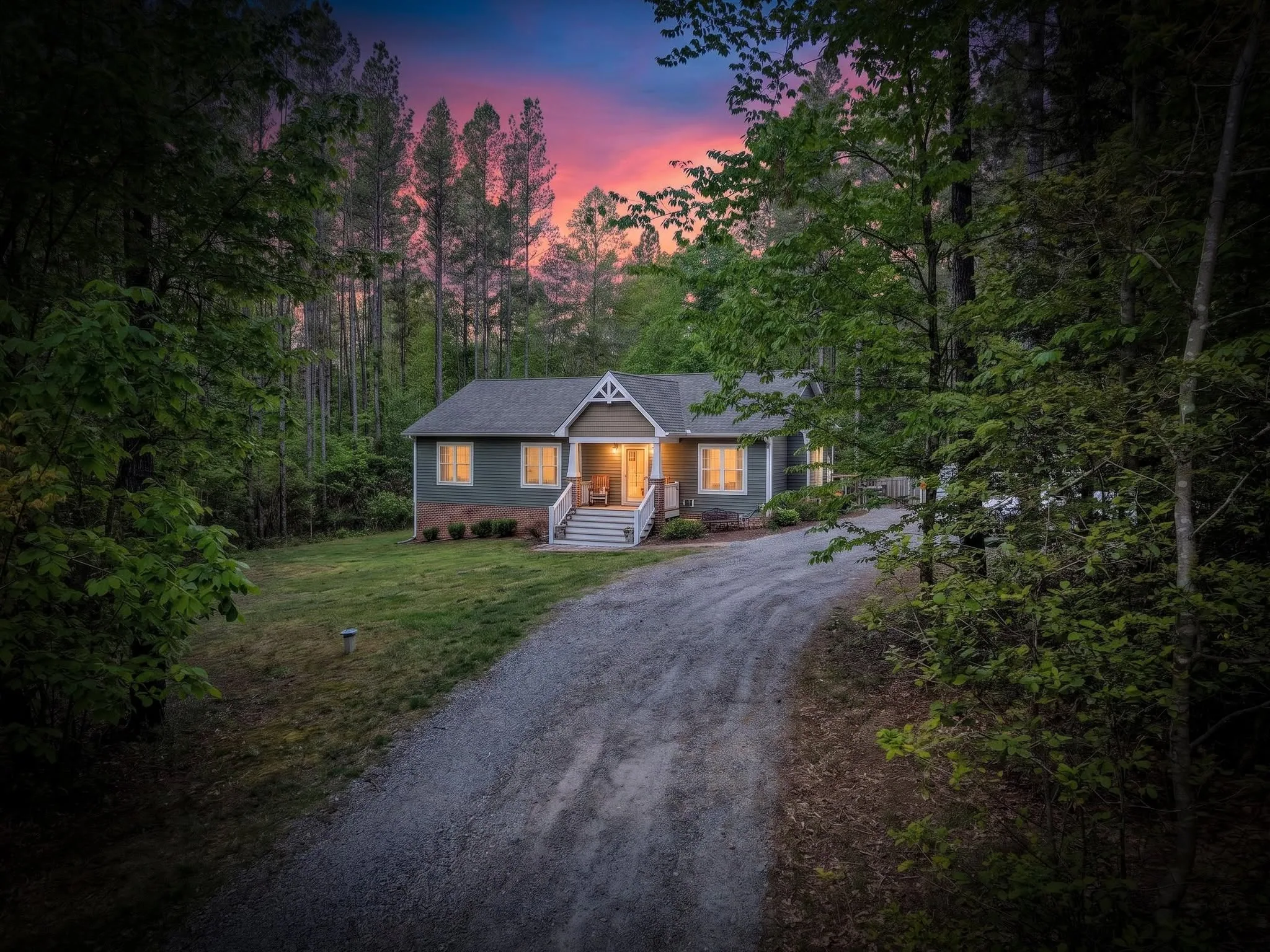 Virtual Twilight image of a home at the end of a gravel drive framed by tall pines under a pink and blue sky