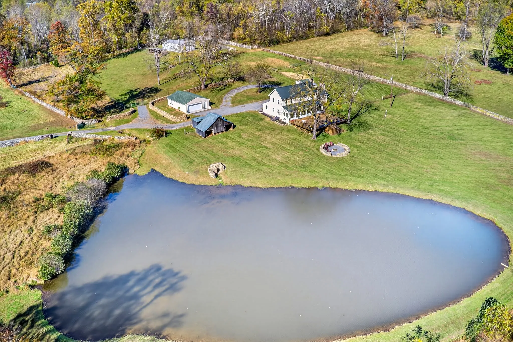 Aerial view of a farm property with a large pond, fenced pasture and a winding drive