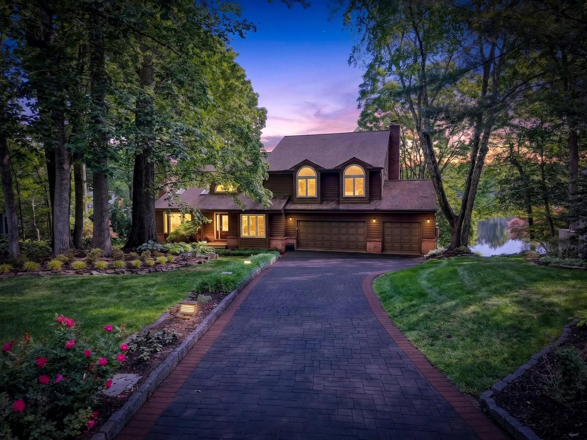 Residential home photographed at twilight with warm interior light and a lit driveway approach