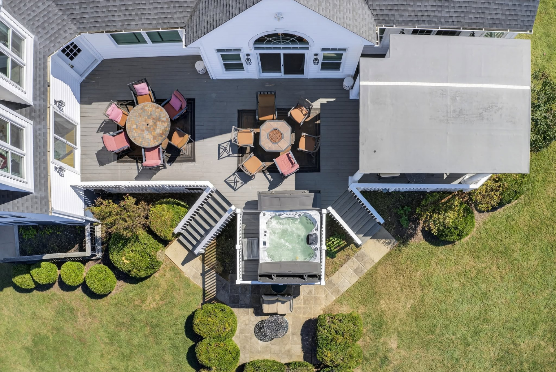 Top-down aerial view of a home’s deck with outdoor tables and seating, stairs, and a nearby hot tub.