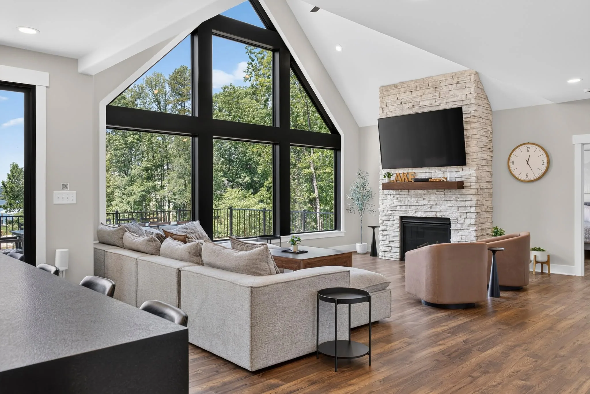 Vaulted living room with black-framed windows, a stone fireplace and a low sectional