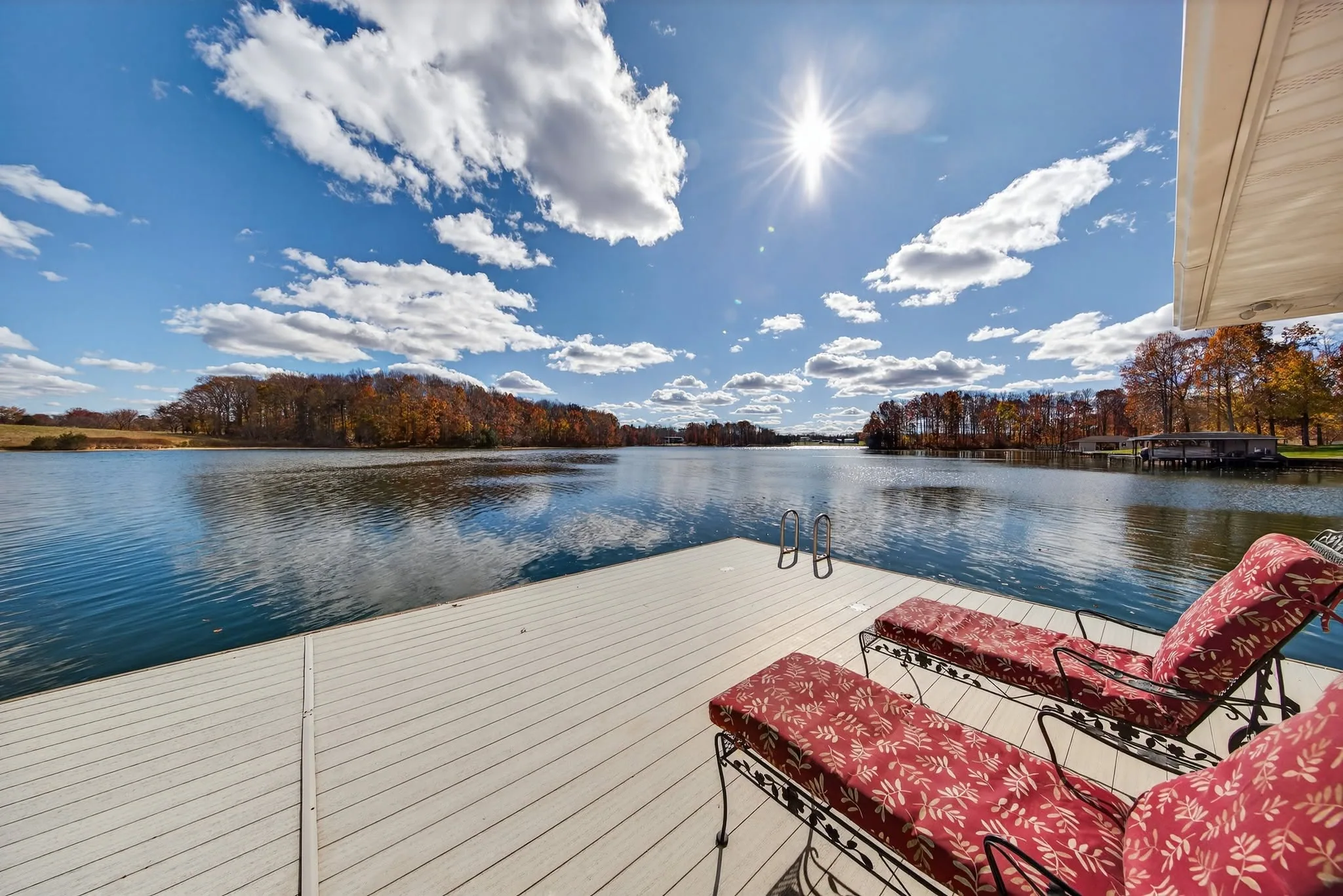 Cushioned loungers on a white dock looking out across open lake water under a bright sky