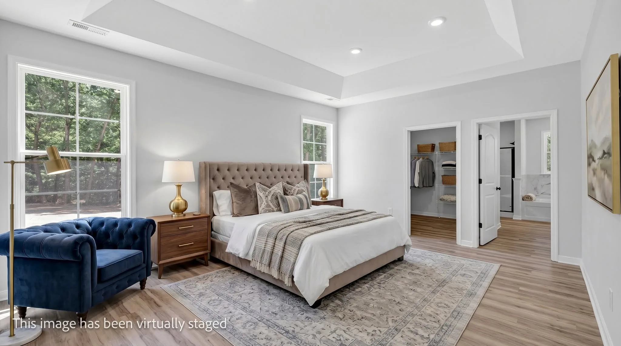 Virtually staged primary bedroom with an upholstered bed, velvet armchair and area rug